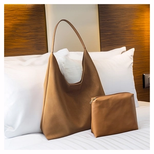 Detailed view of brown leather tote bag set with matching zipper pouch on white bedding