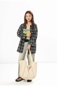 Close-up of oversized cream canvas tote bag paired with a classic plaid flannel shirt