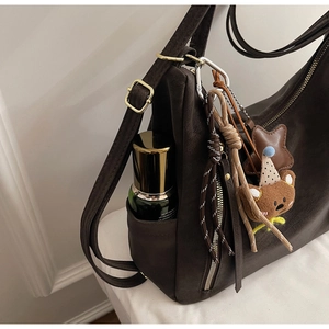 Detail view of coffee brown tote side pocket with plush bear charm and gold hardware