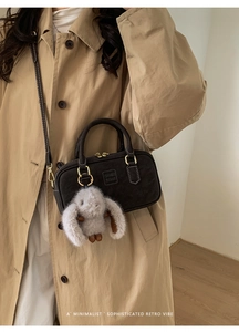 Detail of dark brown suede bowling bag with cute plush bunny pendant and gold hardware