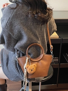 Brown faux leather crossbody bag with teddy bear charm and scarf on a model