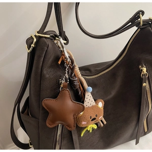 Detail of dark brown leather tote featuring gold zippers and cute bear plush charm