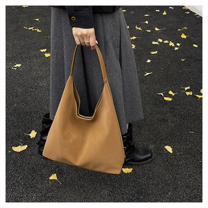 Brown leather hobo tote bag held outdoors over autumn ginkgo leaves on asphalt