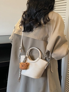 Elegant off-white half-moon handbag with a cute teddy bear charm and adjustable strap