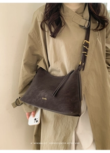 Detail of minimalist dark coffee dumpling bag featuring golden brand logo and buckled strap