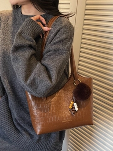 Brown crocodile embossed tote bag with fuzzy pendant carried by a model in knitwear