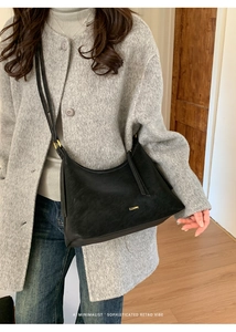Close-up of black hobo shoulder bag with golden brand logo on a grey wool coat