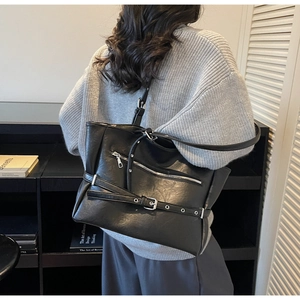 Model wearing a black faux leather underarm bag with zipper and buckle details indoors