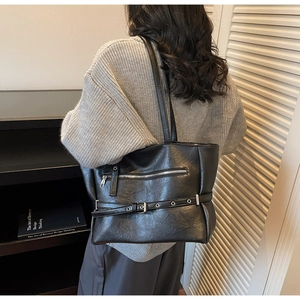 Detail of the black leather tote bag showing the side zipper and silver buckle accents