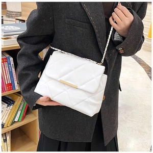 Close-up of white quilted leather crossbody bag with gold chain strap in a library setting