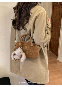 Brown retro bowling bag with plush rabbit charm shown on a model in a cozy interior