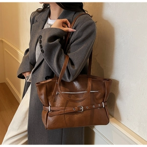 Detail of a brown leather tote bag with silver zippers and metal rings on a model