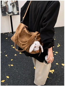 Detail der braunen Vintage-Tasche mit Plüsch-Hasenanhänger und breitem Griff auf Ginkgoblättern