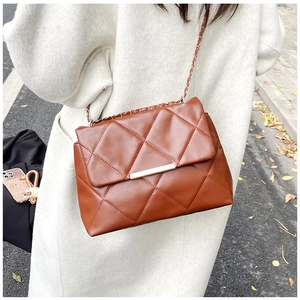 Close-up of brown quilted crossbody bag with chain strap worn over a beige coat