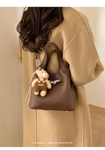 Detail of dark brown lychee leather bucket bag with silver lock and cute bear charm