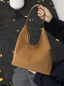Brown vintage hobo tote bag held by hand over autumn leaves on ground for women