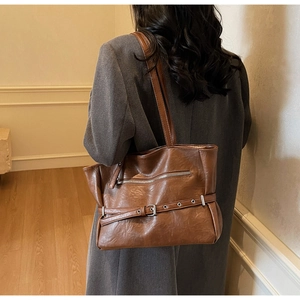 Detailed view of brown faux leather tote bag featuring a decorative belt buckle and zipper