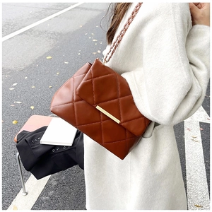 Detail of brown quilted chain bag with gold metal clasp and woven leather strap