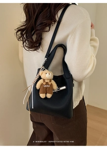 Detail of black pebbled leather bucket bag with a cute brown teddy bear bag charm