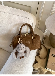 Detail of dark brown suede Boston bag with embossed logo and cute rabbit charm accent