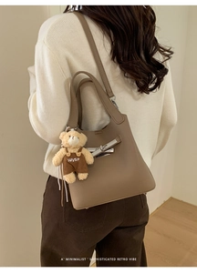 Close-up of textured grey-brown grained leather bucket bag with silver twist-lock and bear toy