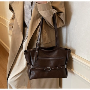 Detail of dark brown leather tote bag showing decorative buckles and zip pocket