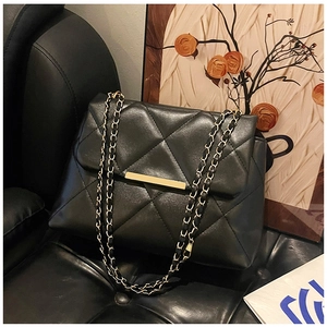 Close-up of black quilted leather handbag with gold metal clasp on a leather sofa