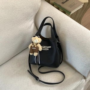 Detail of black lychee grain bucket bag with cute plush bear charm on beige sofa