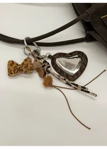 Detail of leopard print bow and heart charm keychain on a brown leather tote bag