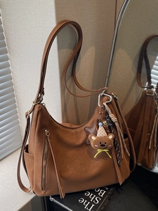 Brown vintage hobo tote bag with fringe detail and cute bear charm in warm indoor setting