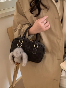 Deep grey matte Boston bag with plush rabbit charm worn with a stylish trench coat
