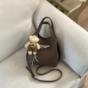 Detail of dark brown litchi pattern leather bucket bag with silver metal lock and teddy charm