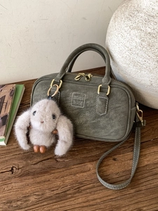 Green bowling bag in vintage matte leather with plush rabbit charm on a wooden surface