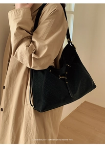 Detail view of large black woven tote bag with gold hardware on a beige trench coat