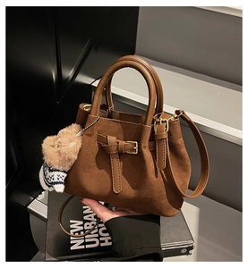 Detail of brown suede bucket bag featuring a leather strap and a cute bear plush charm
