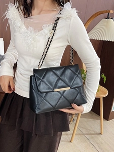 Elegant black quilted crossbody bag with gold chain strap worn by model in cozy interior