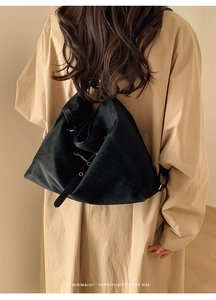 Detail of black woven tote bag with Intrecciato texture worn on a beige trench coat