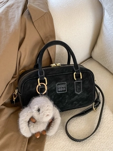 Retro black bowling handbag with plush rabbit charm and adjustable shoulder strap on a sofa