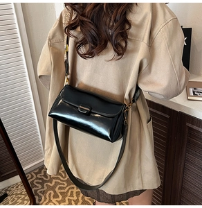 Detail of minimalist black patent leather shoulder bag with sleek metal buckle on a model