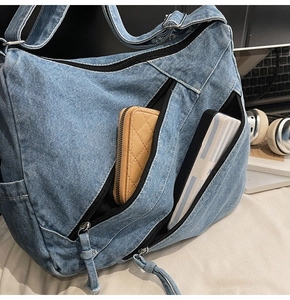 Detail of light blue washed denim shoulder bag with multiple zippered pockets and large capacity