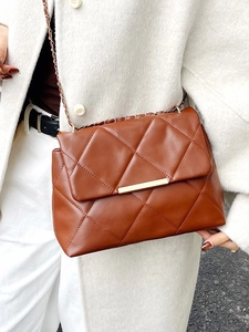 Brown quilted crossbody bag with gold chain strap and metallic lock on white coat