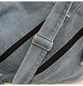 Close-up of adjustable denim shoulder strap with silver square buckle and black zipper details
