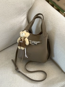 Brown litchi leather bucket bag with metal clasp and plush bear charm on a soft sofa