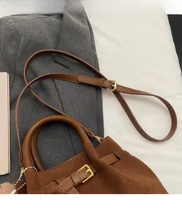 Detail of brown suede bucket bag featuring golden buckle hardware and sturdy top handle