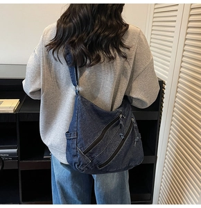 Detail of dark blue denim hobo bag featuring three decorative diagonal zipper pockets