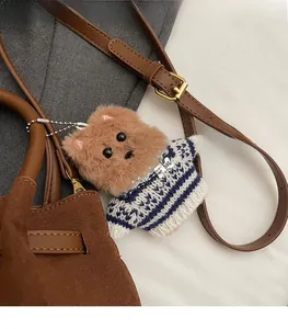 Detail of plush brown puppy bag charm with striped sweater and metal chain on tote