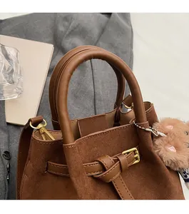 Detail of round handle and suede texture on dark brown bucket bag with plush charm