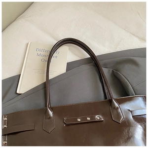 Detail of dark brown patent leather tote with silver rivets and belt buckle accents