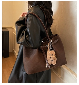 Detail of dark brown tote bag featuring woven texture and plush dog pendant