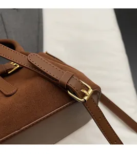 Detail view of adjustable leather strap with brass buckle on a brown suede bucket bag